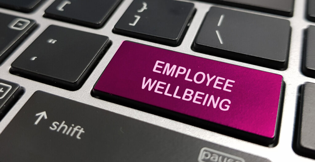 Finger pressing a keyboard key with the words "Employee Wellbeing" printed on the key