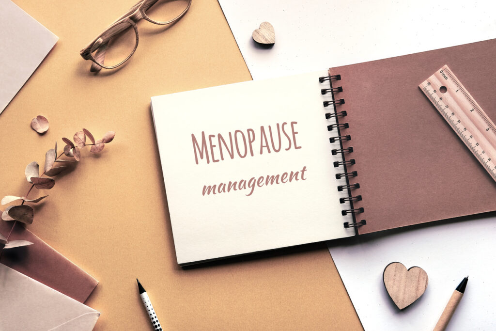 Caption motivator text Menopause management in square album, notebook with spiral binder. Wooden pen, dry eucalyptus twig, wooden heart shape. Soft natural light. Monochromatic beige color hues.